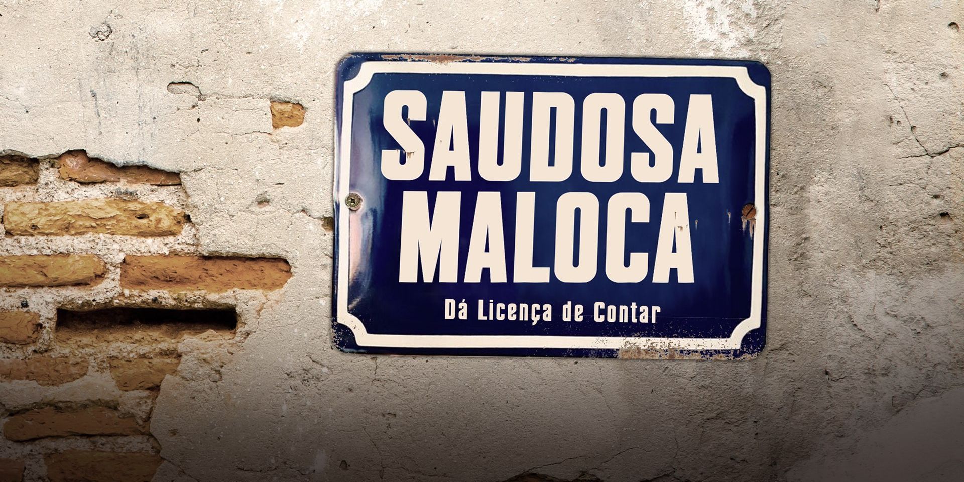 Placa esmaltada azul com o título Saudosa Maloca e o subtítulo Dá Licença de Contar, pregada num muro de reboco descascado com tijolos aparentes