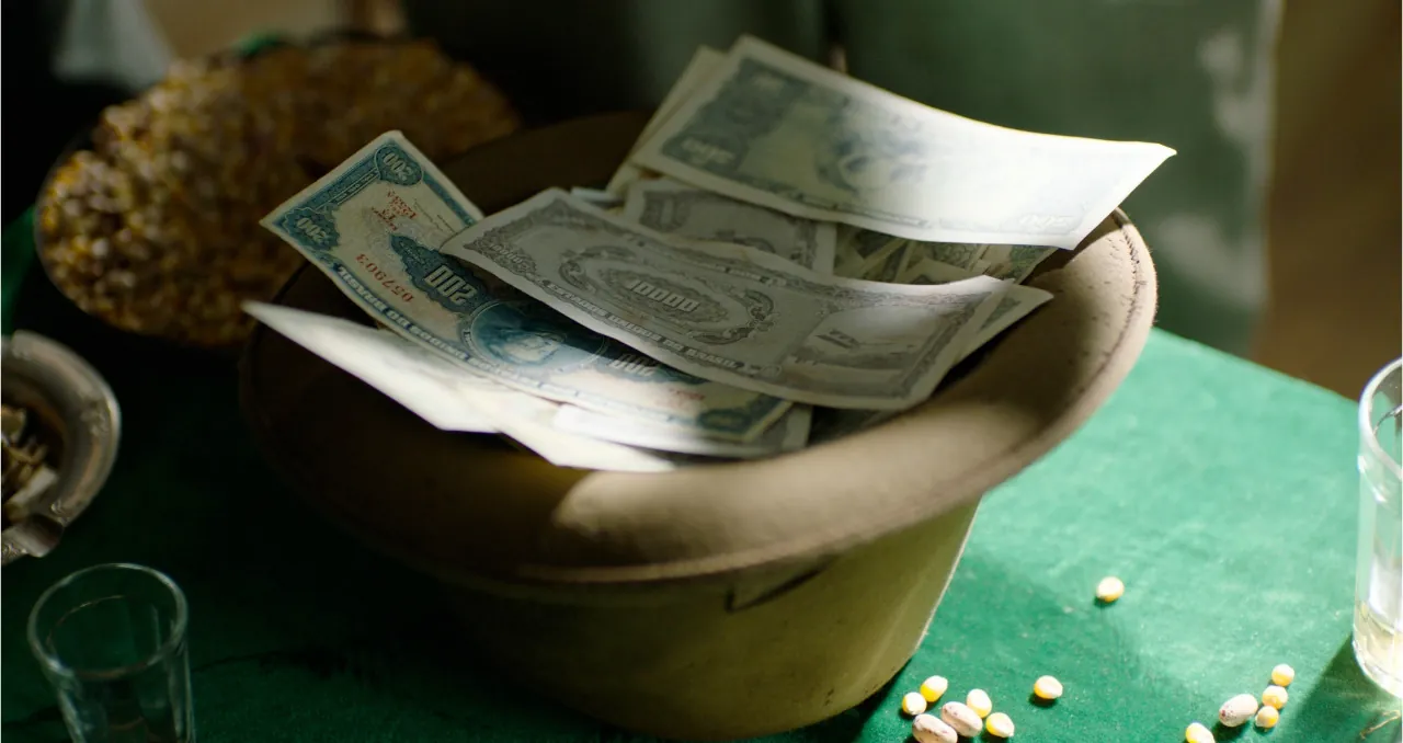 Frame da filmagem: cédulas de cruzeiro dentro de um chapéu sobre uma mesa de jogo verde